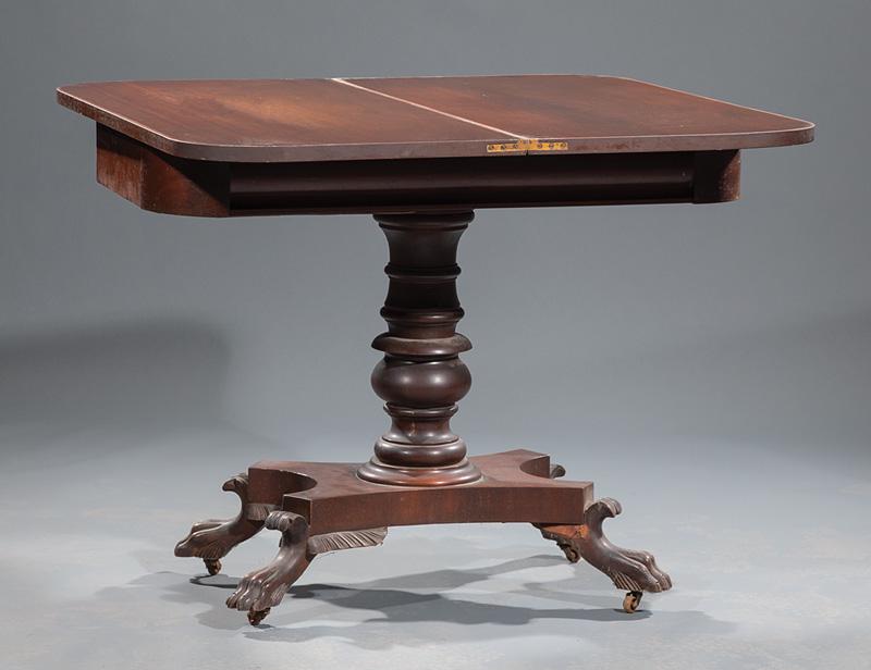 American Classical Carved Mahogany Games Table: American Classical Carved Mahogany Games Table , mid-19th c., Philadelphia, fold-over swivel top, bolection frieze, turned standard, incurvate plinth, winged paw feet, casters, h. 29 in., w. 35 1/2 in