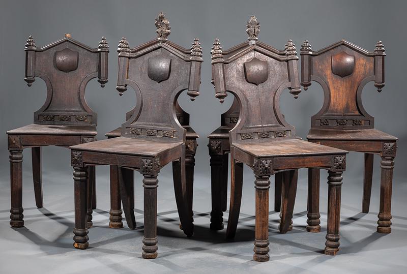Six Oak Hall Chairs: Six American or English Renaissance Revival Oak Hall Chairs , mid-19th c., Gothicized backs centered by shield, finialed crests, trapezoidal plank seat, chamfered legs topped by rosettes, turned feet,