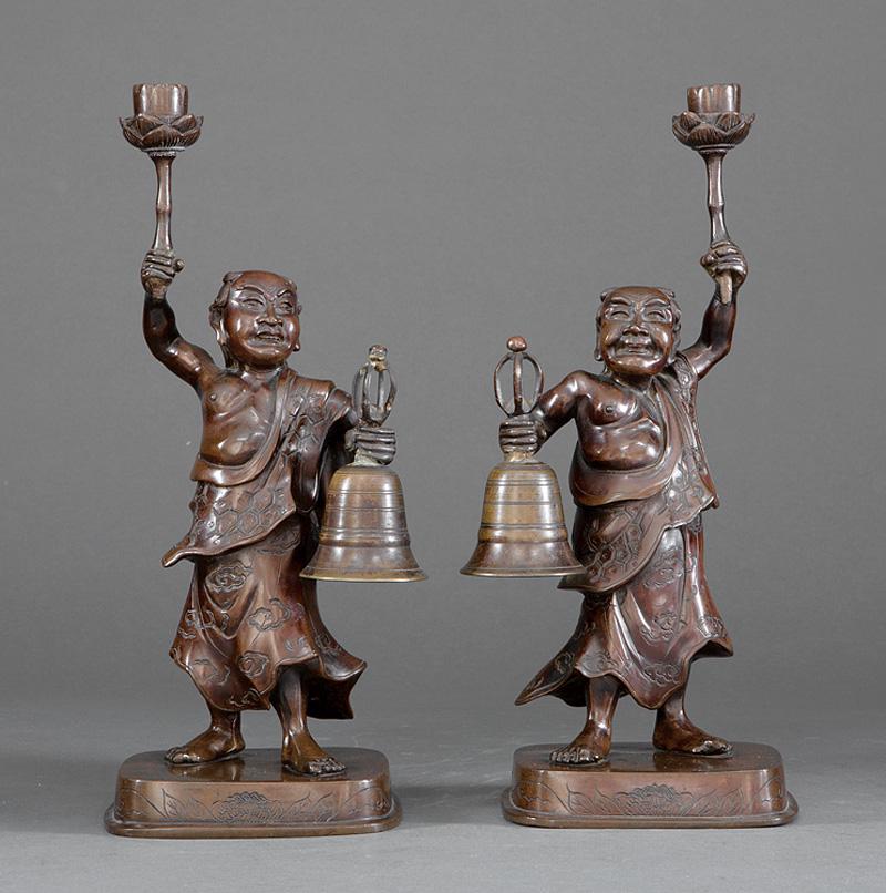 Pair of Japanese Bronze Figural Candle Holders: Pair of Japanese Bronze Figural Candle Holders , each modeled in mirror image with the figure of a partially robed man holding a large bell in one hand and a lotus-form candle holder in the other, h. 