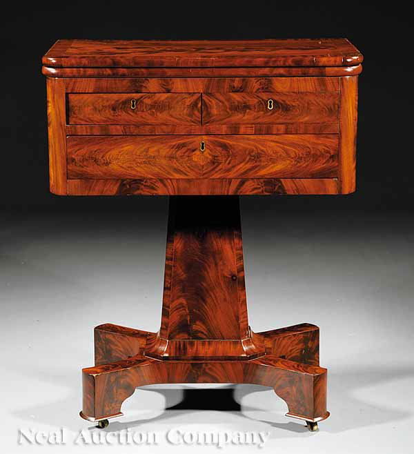 American Classical Work Table, probably Phyfe: An American Classical Figured Mahogany Work Table, c. 1825-1830, probably Duncan Phyfe, New York, having a cross-banded fold-over swivel top above two short and one long drawer, chamfered stem on a pl
