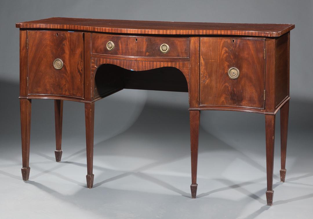 Hepplewhite-Style Mahogany Serpentine Sideboard: Hepplewhite-Style Mahogany Serpentine Sideboard , central drawer, side cabinets, tapered legs, spade feet, h. 35 3/4 in., w. 60 in., d. 22 3/4 in . Condition: AS IS, should be viewed in person. Chips,