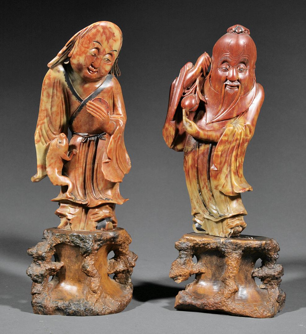 Two Chinese Carved Soapstone Figures: Two Chinese Carved Soapstone Figures of Immortals , each figure raised on a naturalistic carved stone base, the first depicted holding a peach, the second, with a three legged toad, h. 13 7/8 in. and 