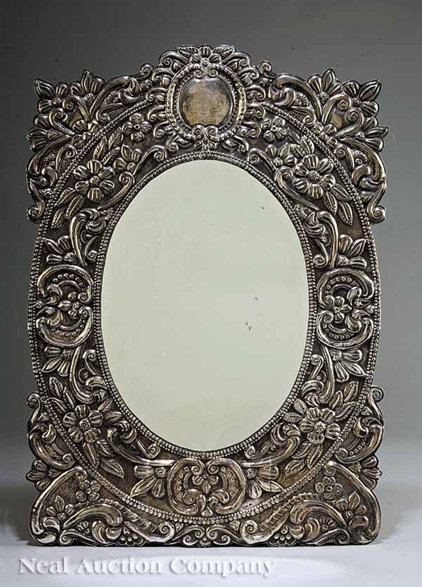 Latin American Silver Repousse Wall Mirror: An Antique Latin American Silver Repousse Wall Mirror, late 19th c., stamped "900" and "ARE 04", cartouche crest, foliate frame, oval beaded inner molding, height 23 in., width 16 in