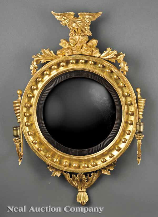 Regency Giltwood Bullseye Mirror: A Regency Giltwood Bullseye Mirror , c. 1805, surmounted by a spread wing eagle on rockwork base issuing acanthus, circular mirror frame with spherules and an ebonized rabbet, convex mirror plate, bee