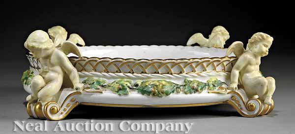 A Minton Polychrome Porcelain Center Bowl: A Minton Polychrome and Gilt-Decorated Porcelain Center Bowl, central oak leaf and acorn molded band, four outswept scroll feet surmounted by winged putti, claret stamp, gilt number "G.A. 1394", heigh