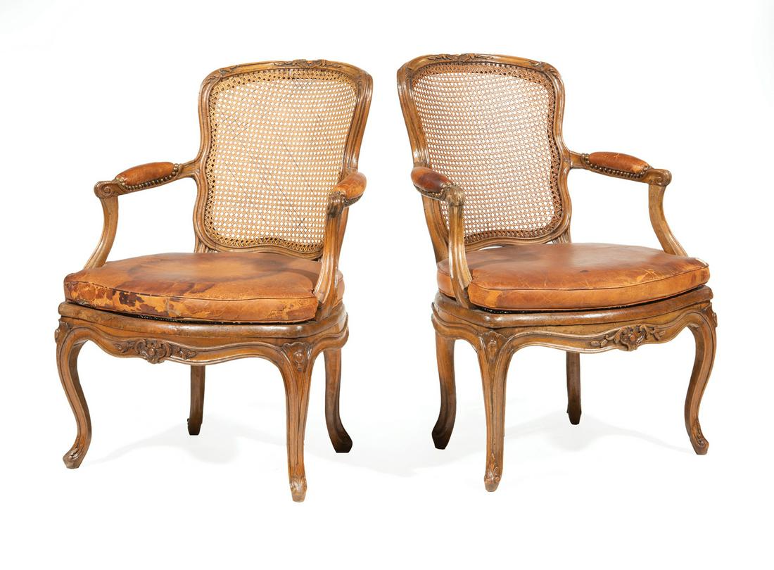 Louis XV-Style Carved Fruitwood Fauteuils: Pair of Antique Louis XV-Style Carved Fruitwood Fauteuils, possibly 18th c., floral crest rail, caned back, scrolled arms, leather cushions, serpentine seat rail, cabriole legs, h. 34 in., w. 24 in.,