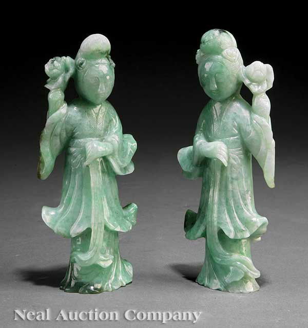 Chinese Jadeite Figures of Meiren: A Near Pair of Chinese Jadeite Figures of Meiren, each beauty carved wearing long robes and carrying a lotus blossom in one hand, the serene down turned faces framed by high chignons, height 5 3/4 in.