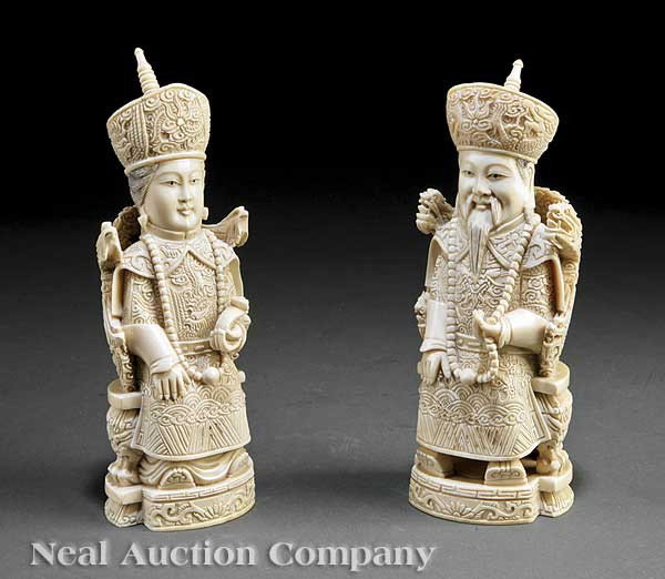 Pair Chinese Ivory Emperor and Empress Figures: A Pair of Chinese Ivory Emperor and Empress Figures, the male figure carved seated on a dragon throne wearing dragon robes cradling a bead necklace in one hand, the female carved seated on a phoenix t