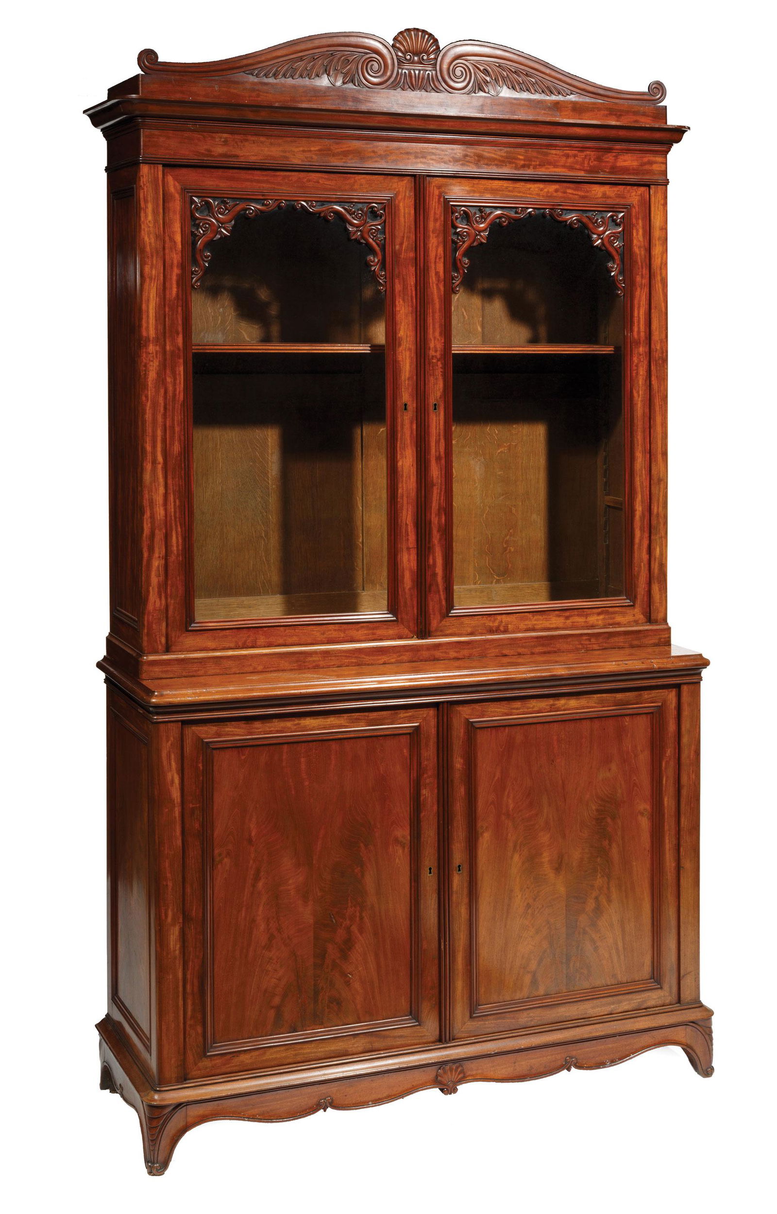 Large William IV Carved Mahogany Bookcase: Large William IV Carved Mahogany Bookcase, mid-19th c., scroll and shell carved pediment over glazed doors, lower case with paneled doors, carved apron, scrolled feet, plum pudding veneers throughout,