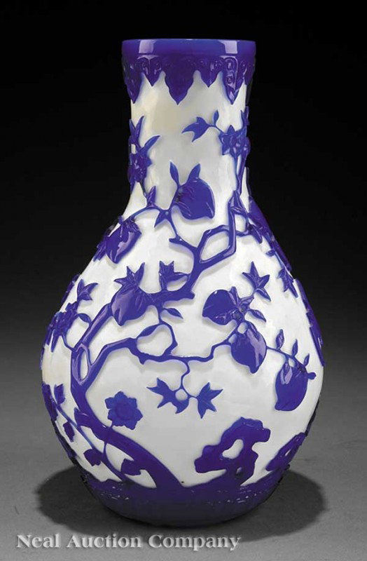 Chinese Beijing Glass Bottle Vase: A Chinese Beijing Glass Bottle Vase, probably early 20th c., deeply carved through the blue overlay to a milky white ground with bats, flowering prunus blossoms, and peaches, height 11 1/2
