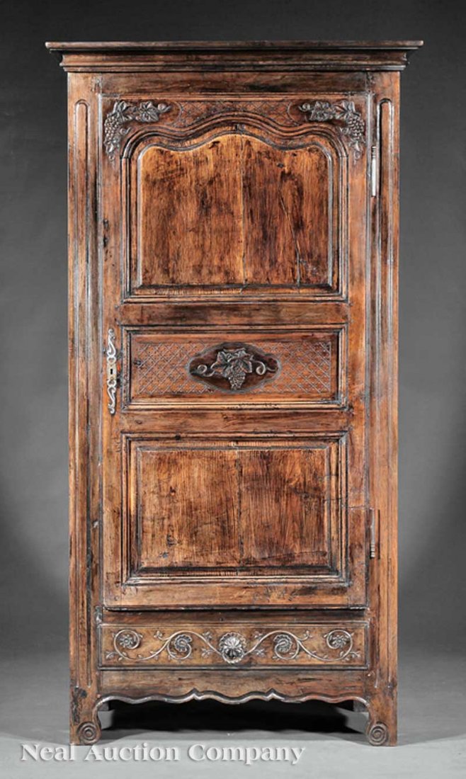 French Provinçial Carved Walnut Bonnetière: A French Provinçial Carved Walnut Bonnetière, early 19th c., Normandy, molded cornice over a paneled door embellished with grape clusters, above a vine and floral carved drawer, shaped apron, bracke