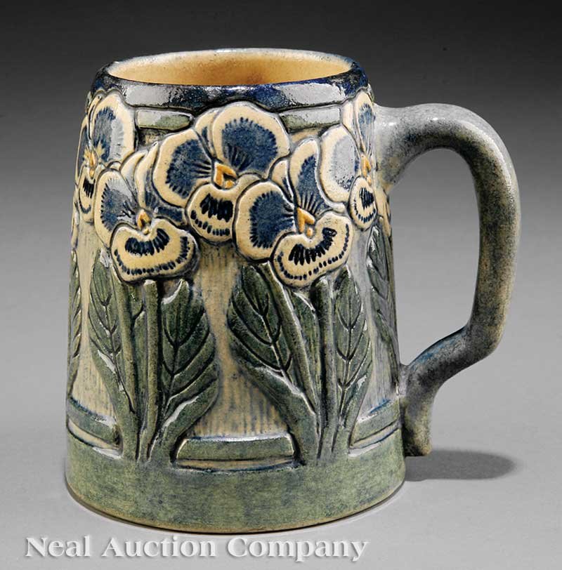 Newcomb College Art Pottery High Glaze Tankard: A Newcomb College Art Pottery High Glaze Tankard, 1907, decorated by Mary Louise Dunn in a relief-carved pansy motif, dark blue, green and mustard yellow underglaze, base marked with an effaced Newcom