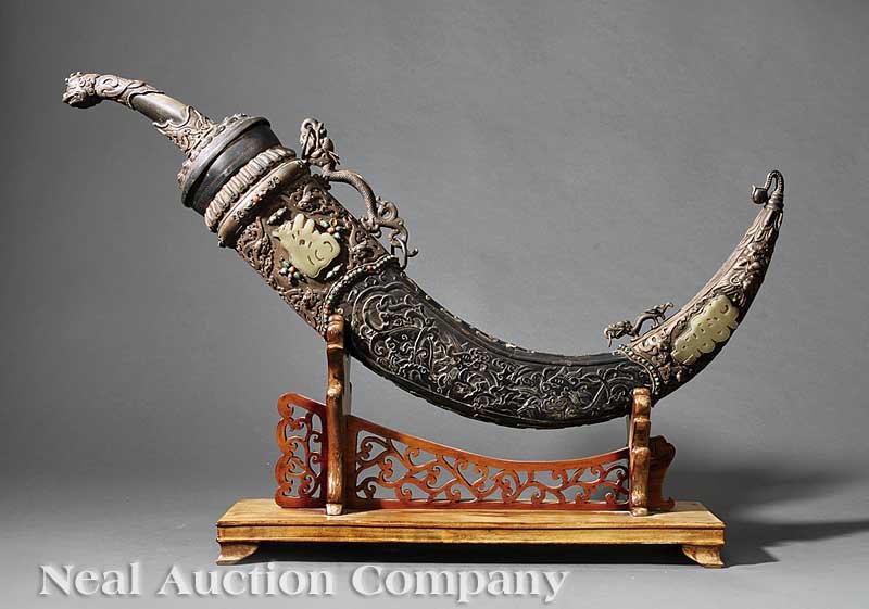 A Chinese/Mongolian Dagger and Scabbard: A Chinese/Mongolian Horn, Jade, Hardstone "Gem" and Silver-Mounted Dagger and Scabbard, curved blade, narrow fuller, length 12 5/8 in.; silver guard, canted horn grip, and "gem" inset silver makara he