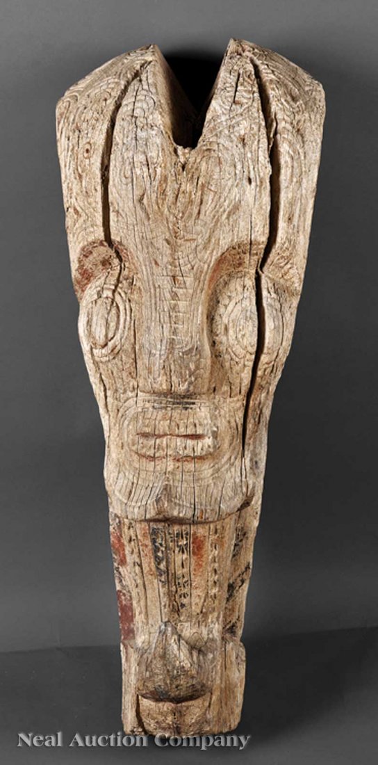 Indonesian Carved Wood Architectural Element: A Monumental Indonesian Carved Wood Architectural Element, Batak, Sumatra, tapering rectangular form carved as a massive head with exaggerated features, a split crown, and a long beard, remnant red an