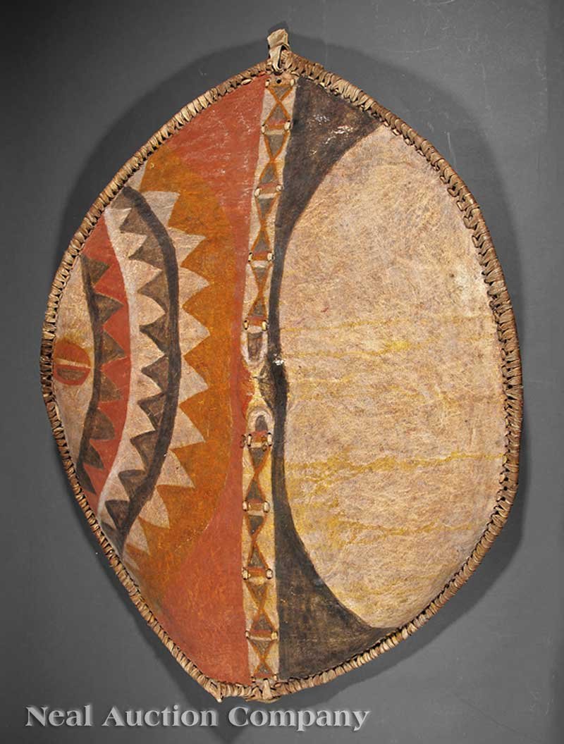 An African Hide Shield: An African Hide Shield, Masai, Kenya, elliptical body with geometric designs, red, yellow, black and white pigment, height 49 1/2 in., width 33 1/2 in., metal hanging mounts Provenance: With Taylor A.