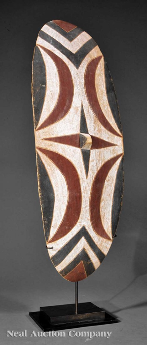 An African Carved Wood Dance Shield: An African Carved Wood Dance Shield, Tutsi, Rwanda, oval form with central pyramidal boss carved with geometric designs, red, black and white pigment, height 33 1/2 in., width 12 in., custom metal sta