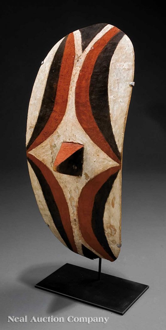 An African Carved Wood Shield: An African Carved Wood Shield, Tutsi, Rwanda, elliptical form with central pyramidal boss, red, black and white pigment, height 23 in., custom metal stand, overall height 26 in. Note: Small loss to ba