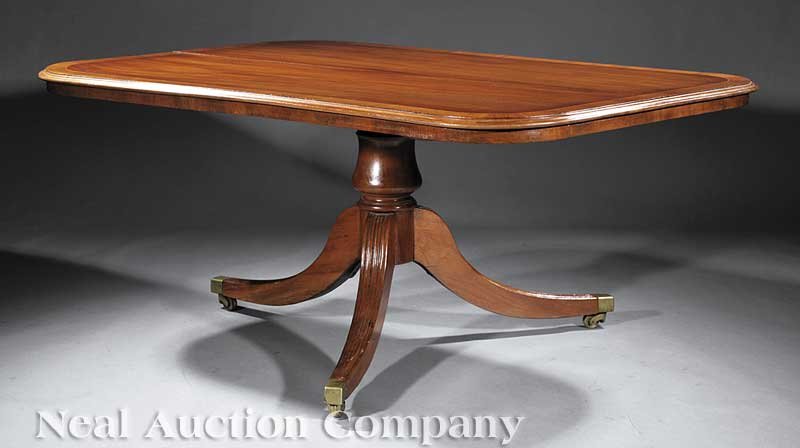 Antique Regency-Style Breakfront Table: A Fine Antique Regency-Style Carved and Inlaid Mahogany Breakfront Table, banded tilt top with molded edge, vasiform support, reeded sabre legs ending in brass casters, height 29 in., length 64 in., w