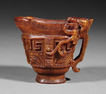 Chinese Carved Rhinoceros Horn Libation Cup: A Small Chinese Carved Rhinoceros Horn Libation Cup, 18th c., carved with two kui dragons clambering over the lip on either side of the flat loop handle, the sides with taotie masks on a squared spira