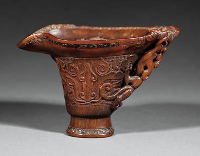 Chinese Carved Rhinoceros Horn Libation Cup: A Chinese Carved Rhinoceros Horn Libation Cup, 18th c., deep body carved with two kui dragons forming the openwork handle, one extending over the everted lip, the sides relief carved with archaistic m