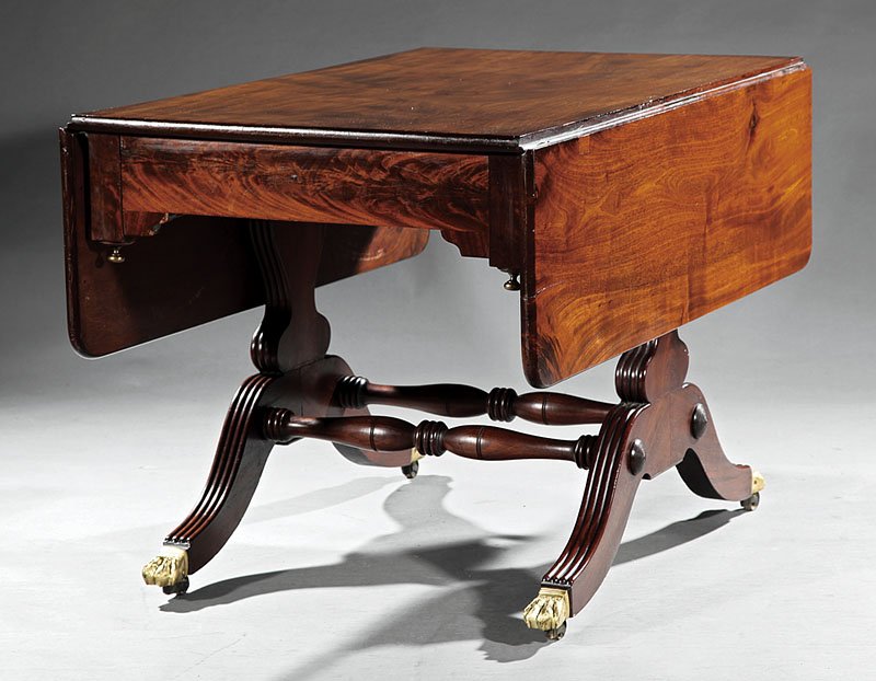 An American Classical Mahogany Sofa Table: An American Classical Carved Mahogany Drop-Leaf Sofa Table, early 19th c., Baltimore, frieze with brass pendant corners, reeded vasiform trestle supports joined by stretchers, outswept legs, brass paw