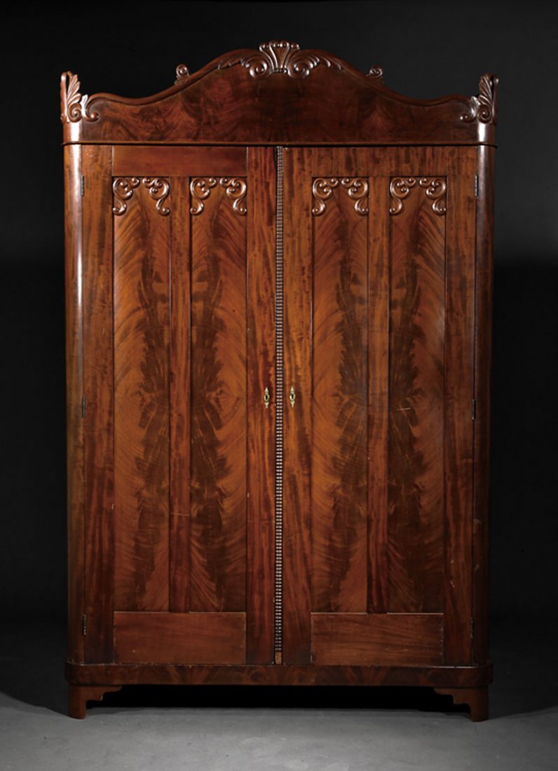 An American Late Classical Mahogany Wardrobe: An American Late Classical Carved Mahogany Wardrobe, mid-19th c., shaped cornice with scrolled acanthus over paneled doors, divided interior with hanging compartment and graduated drawers, plinth base