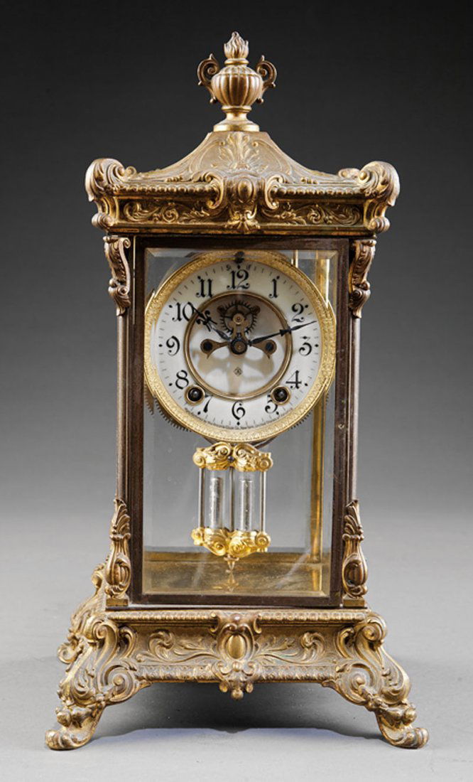 An American Gilt Metal Crystal Regulator Clock: An American Gilt Metal Crystal Regulator Clock, early 20th c., by Ansonia, New York, porcelain dial with visible escapement, case with floral and scroll decoration, height 16 1/2 in., width 8 3/4 in.,