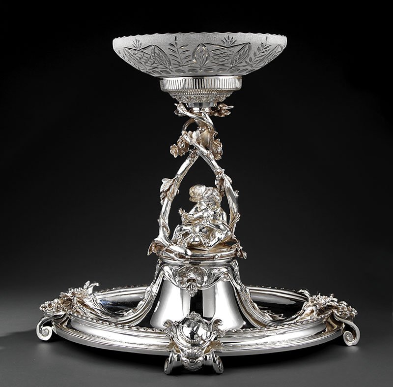 Silverplate Figural Centerpiece: A Monumental Silverplate Figural Centerpiece, cut and etched glass center bowl, on arbor support mounted with putti, segmented oval base, elaborate scroll feet, height 23 in., length 25 in., depth 20 