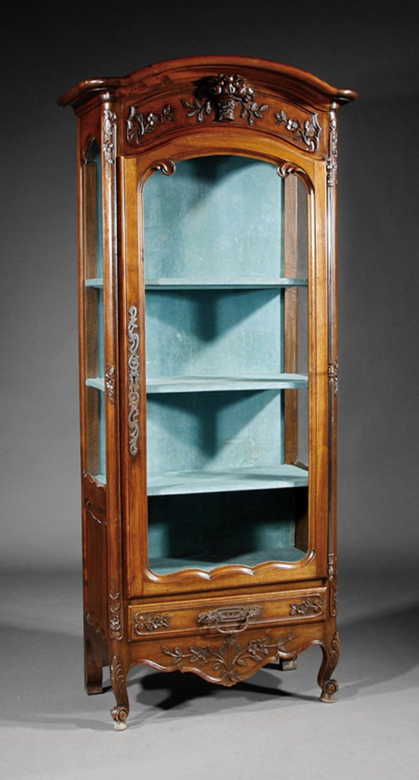 A Louis XV-Style Carved Walnut Vitrine: A Louis XV-Style Carved Walnut Vitrine, 19th c., molded shaped cornice, floral frieze, arched paneled glazed door and sides, shelf interior, single drawer below, cabriole legs, height 74 1/2 in., widt