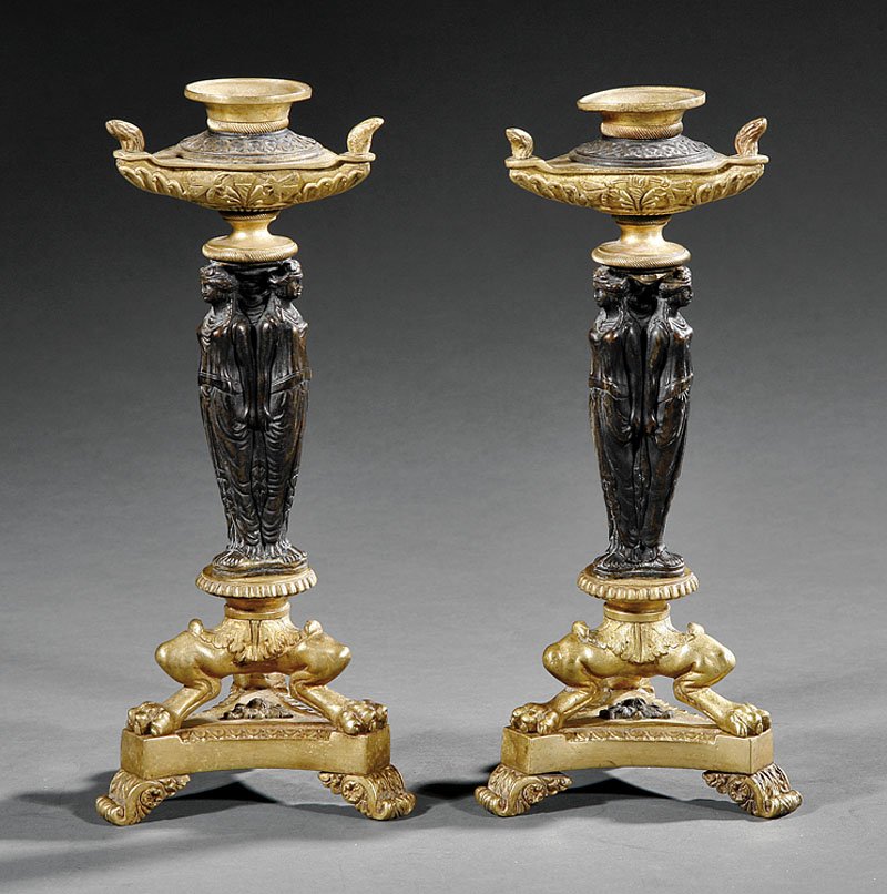 Candlesticks, after the designs of Thomas Hope: A Pair of Regency Gilt and Patinated Bronze Figural Candlesticks, early 19th c., after the designs of Thomas Hope, each candlecup with flame finials atop standard in the form of the three graces, trip