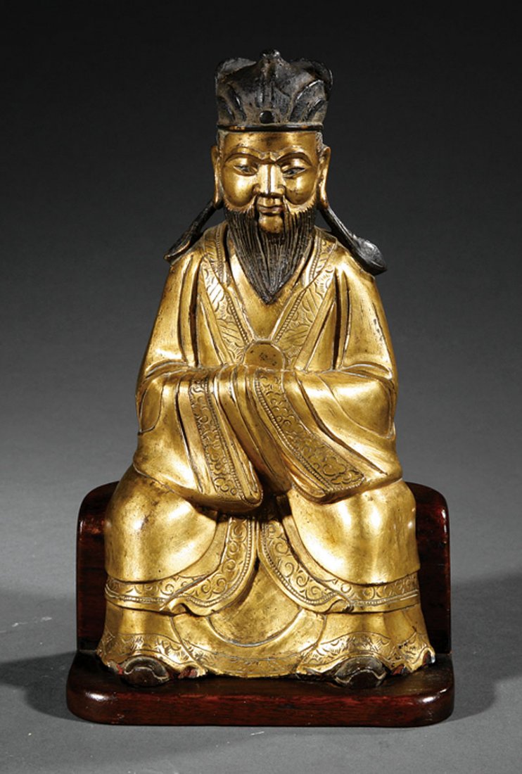 A Chinese Gilt Bronze Figure of an Official: A Chinese Gilt Bronze Figure of an Official, probably Ming Dynasty (1368-1644), seated figure modeled wearing voluminous robes and an official's cap holding a hu tablet before his chest, height 8 3/8 