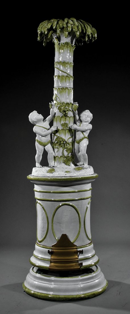Continental Glazed Earthenware Figural Stove: A Continental Glazed Earthenware Figural Stove, cylindrical body surmounted by two putti flanking a palm tree, molded base, gilt bronze paw feet and door, height 87 1/2 in., diameter 23 in