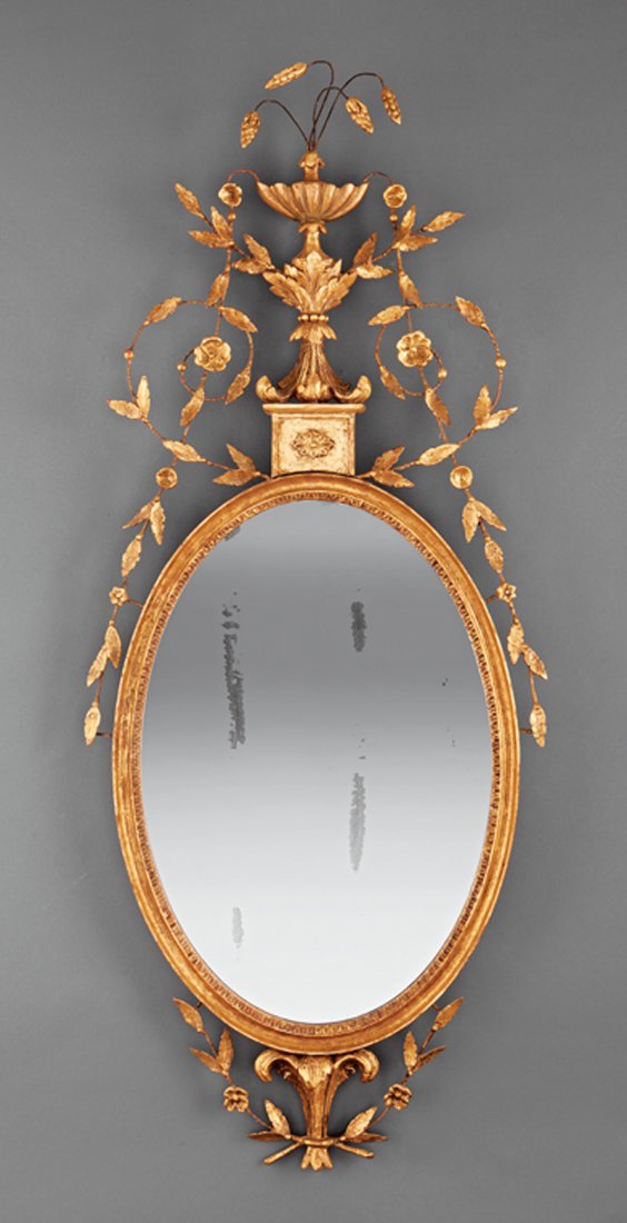 A Pair of George III Carved Giltwood Mirrors: A Pair of George III Carved Giltwood Mirrors, early 19th c., oval mirror plate surmounted by vase cascading leaves and flower buds, height 52 in., width 21 in