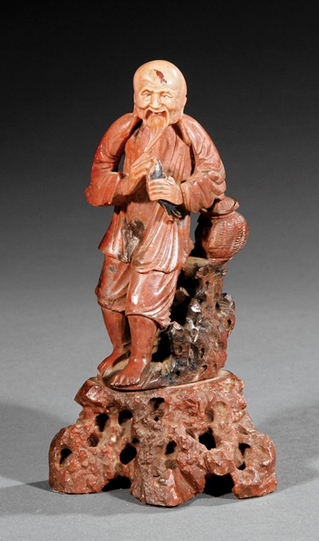 A Chinese Soapstone Figure of a Fisherman: A Chinese Soapstone Figure of a Fisherman, probably 20th c., male figure carved holding a fish standing beside a covered basket atop a rock outcropping, height 6 1/8 in