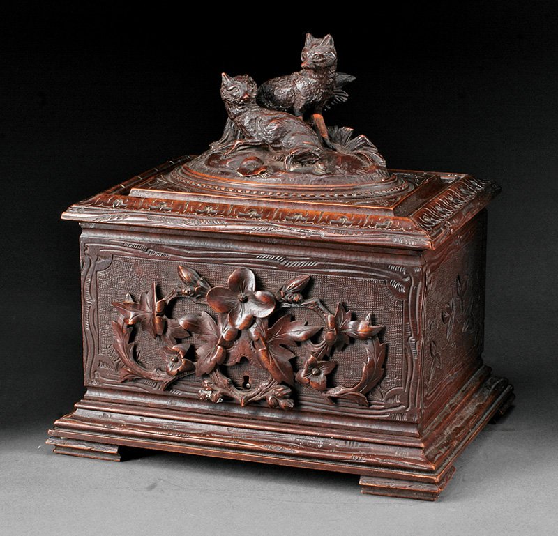 A Continental Black Forest Carved Walnut Humidor: A Continental Black Forest Carved Walnut Humidor, c. 1900, hinged top surmounted by foxes, floral carving on stippled ground, interior with fitted cigar trays, molded base, bracket feet, height 10 1/2