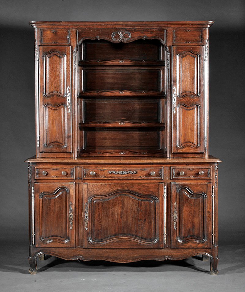 An French Provincial Carved Oak Vaisselie: An Antique French Provincial Carved Oak Vaisselier, 19th c., upper case with molded cornice, scalloped shelves flanked by paneled cupboards, lower case with three drawers over three paneled doors, cab