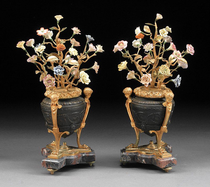 Gilt, Patinated Bronze and Porcelain Urns: A Pair of Louis XVI-Style Gilt and Patinated Bronze and Porcelain Urns, each amphora surmounted by branches, with applied polychrome porcelain flowers, fitted on cherub monopod support, incurvate tria