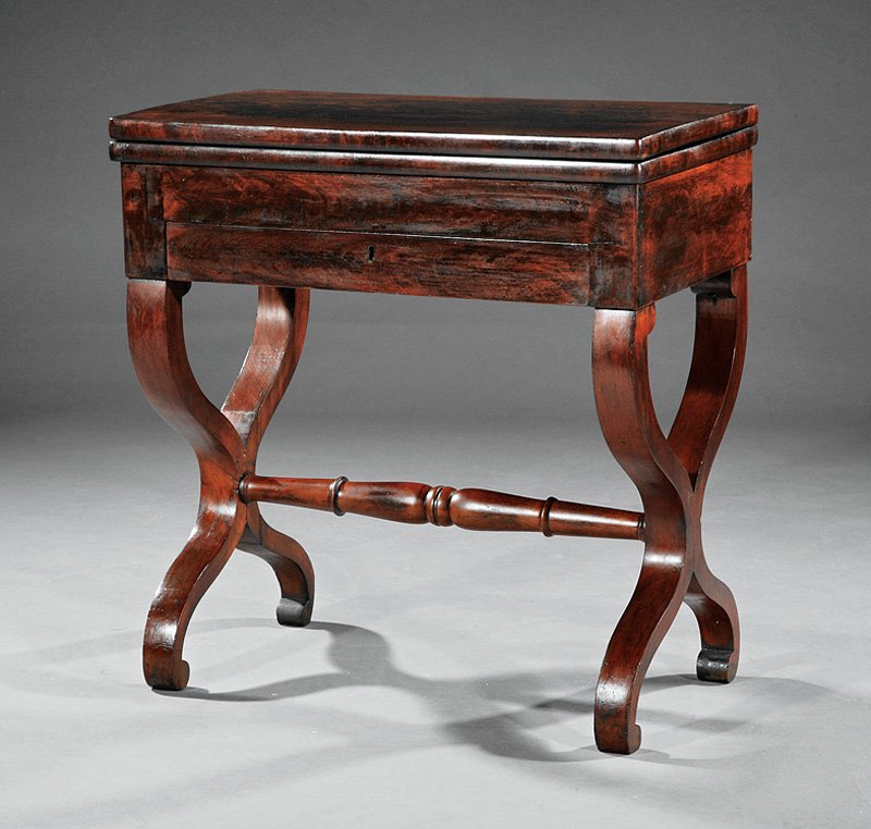 American Classical Carved Mahogany Games Table: An American Classical Carved Mahogany Games Table, early 19th c., New York, foldover baize-lined swivel top, satinwood fitted interior, drawer below, paired scrolled supports, turned medial stretcher,