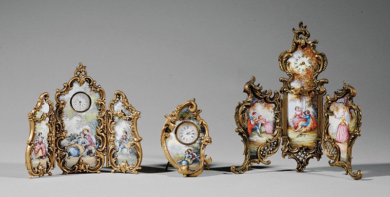 Miniature Gilt Bronze and Enamel Clock Garniture: A Rococo-Style Miniature Gilt Bronze and Enamel Clock Garniture, 19th c., two clocks set within three hinged panel screens, the third clock in a rocaille frame with stand, all decorated with courting 