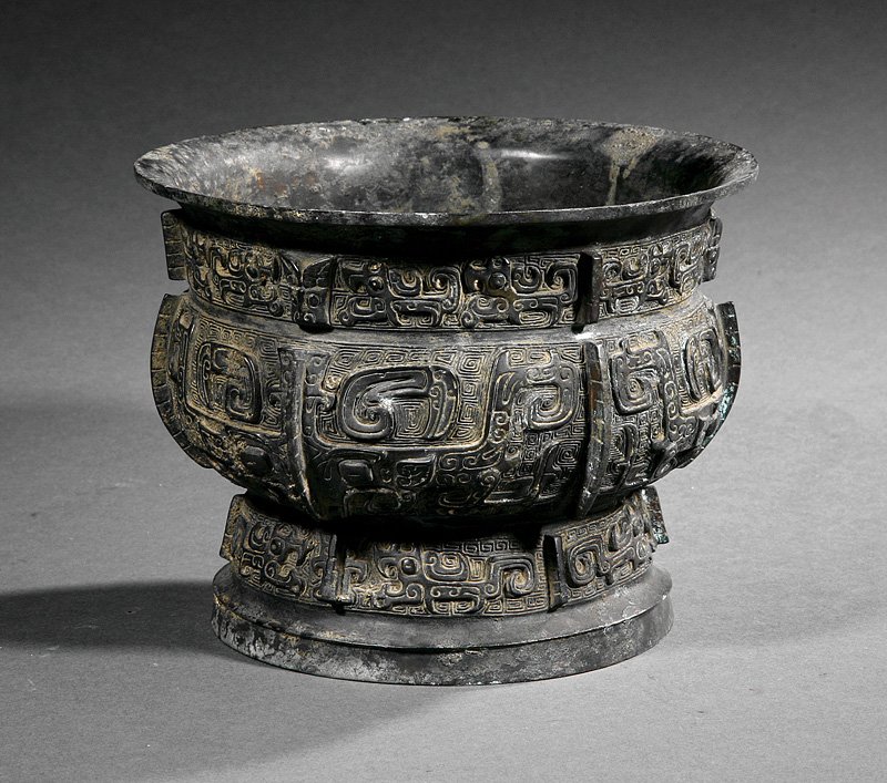 A Chinese Zhou-Style Bronze Vessel: A Chinese Zhou-Style Bronze Vessel, compressed globular body with waisted flared neck and waisted splayed base, relief-modeled around the sides with flanges and archaistic motifs, height 5 1/2 in., di