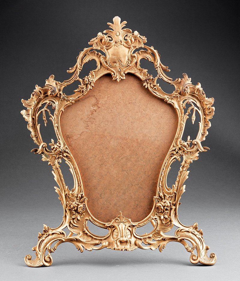 A Louis XV-Style Gilt Bronze Dressing Mirror: A Louis XV-Style Gilt Bronze Dressing Mirror, 20th c., cartouche shape with rocaille decoration, height 23 in., width 17 in. Note: Lacking mirror plate. Provenance: "Villa Rose" Collection of Grace Co