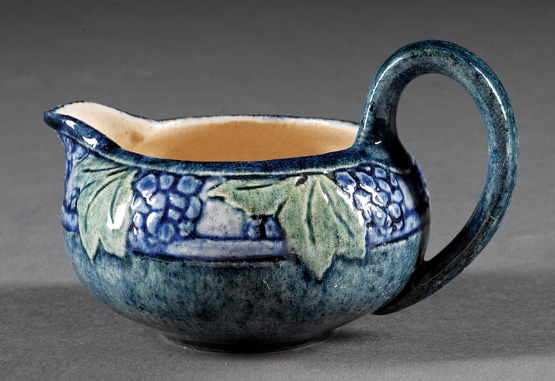 A Newcomb College Art Pottery Creamer: A Newcomb College Art Pottery Creamer, 1907, decorated by Sadie Irvine in low relief with grapes and foliage, high glaze with blue and green underglaze, base marked with Newcomb cipher, decorator's ma