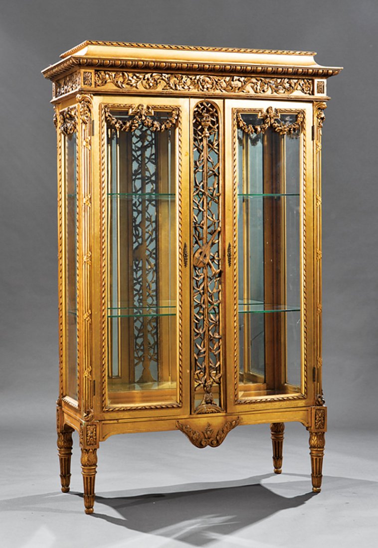 Louis XVI-Style Carved and Gilded Vitrine: Louis XVI-Style Carved and Gilded Vitrine, late 19th c., stepped cornice, swagged beveled glass doors, musical trophee center stile, mirrored back, tapered stop-fluted legs, h. 70 in., w. 44 in., d. 1