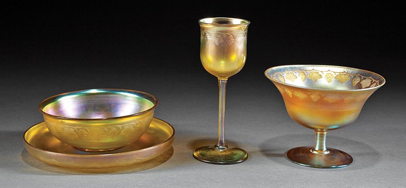 Four Tiffany Favrile Glass Table Articles: Four Tiffany Favrile Glass Table Articles, each marked, grapevine intaglio cut design, incl. dessert coupe, cordial and small bowl with underplate, tallest h. 5 1/2 in., (4 pcs.) Provenance: New Orlea