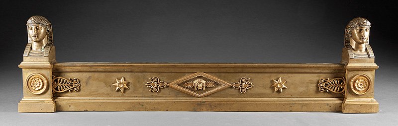 French Empire Gilt Bronze Fireplace Guard: French Empire Gilt Bronze Fireplace Guard, 19th c., in the Egyptian taste, plinth standards surmounted by sphinx busts, mask and foliage relief decorated central cartouche, h. 11 in., w. 42 in., d. 3 