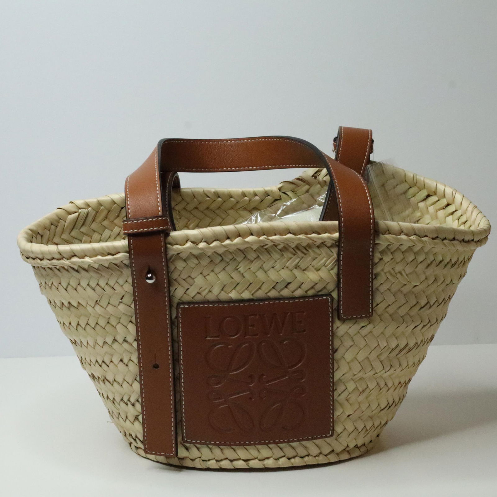 LOEWE PALM LEAF BASKET BAG: Loewe Palm Leaf basket bag in good condition. It features calfskin leather handles and comes with its original dust bag. Details and measurements: Length: 13.75 IN. Height: 7.25 IN. Depth: 5.25 IN. Ha