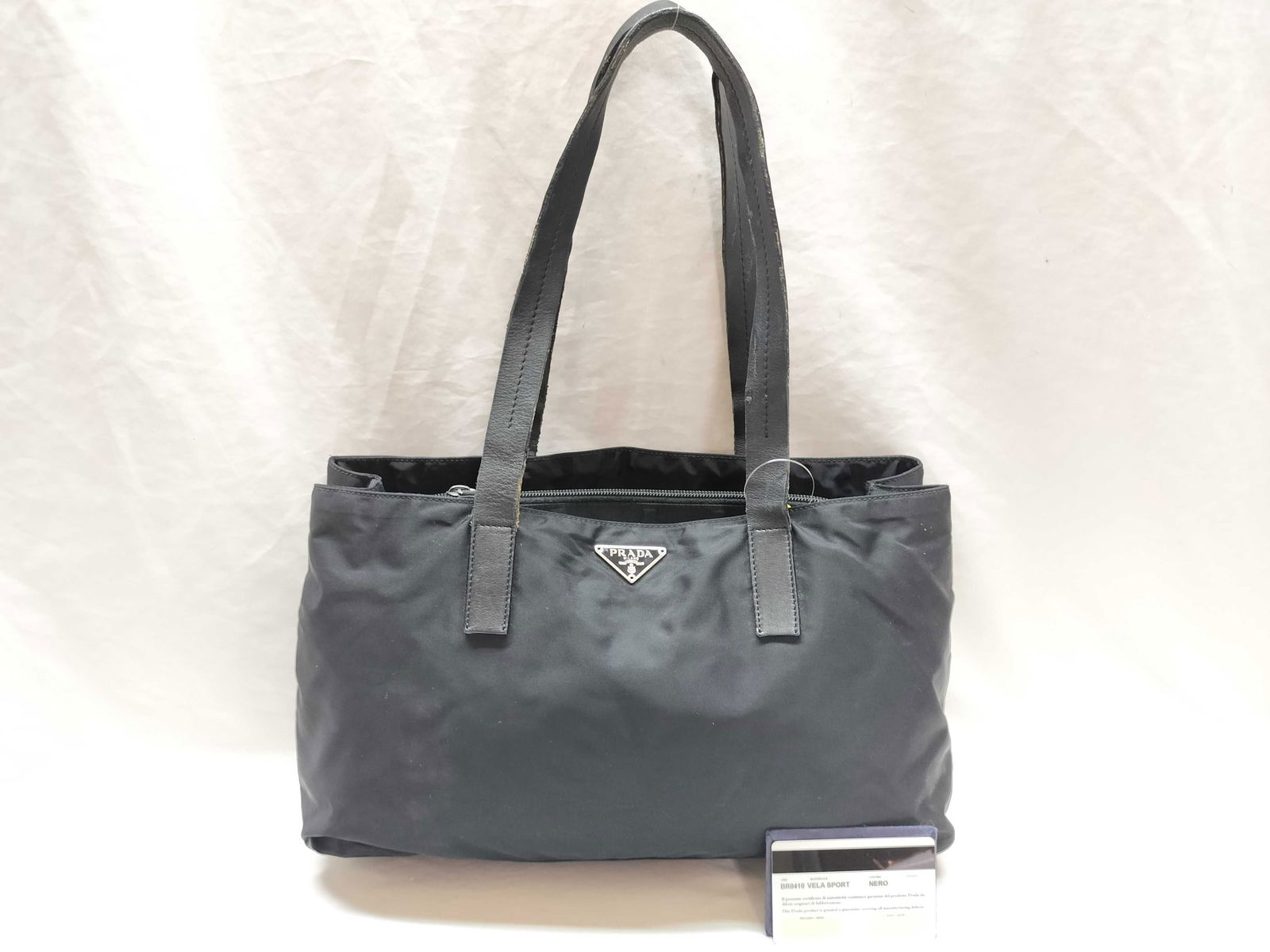 Prada Black Nylon Shoulder Tote Bag: authentic prada tote bag in black nylon with matching leather handles and silver-tone hardware. features prada triangle logo plate on front and zip top closure. nylon shows light wrinkling, minor fadi