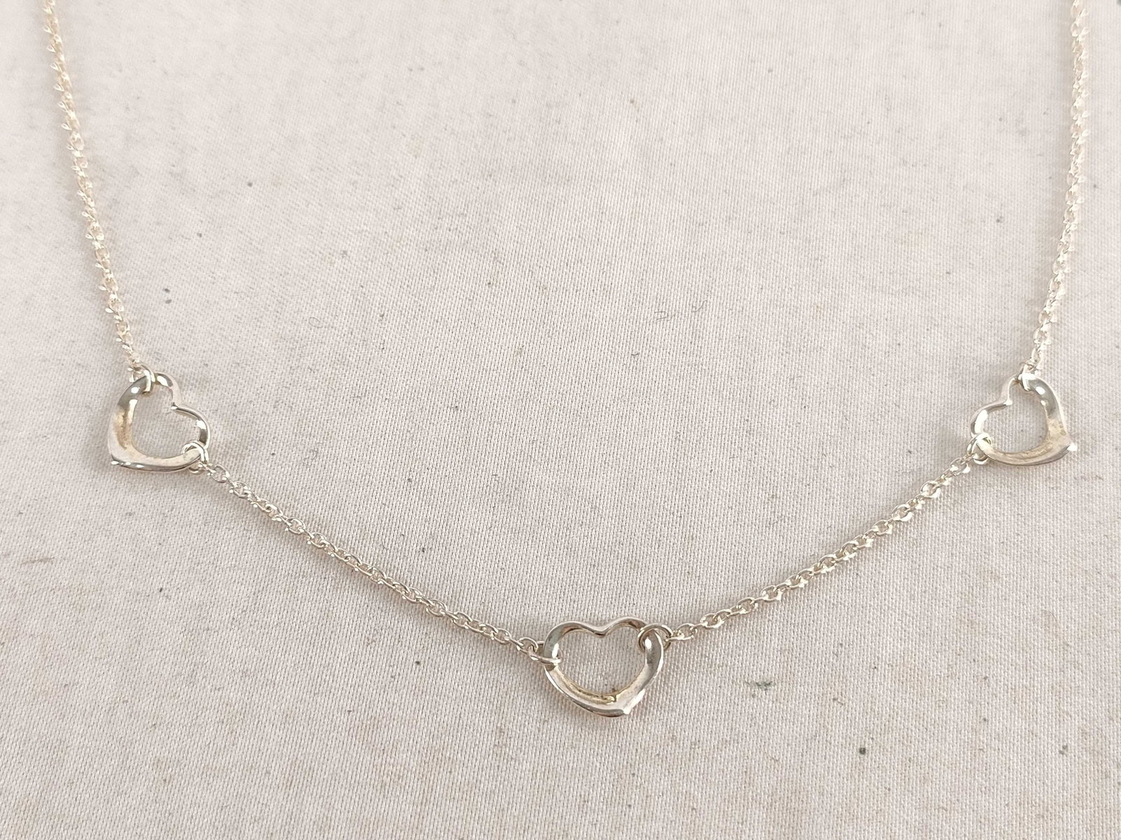 Tiffany & Co. Open Heart Three-Station Necklace: Tiffany & Co. open heart sterling silver necklace having three small open heart stations evenly spaced along fine chain. Hearts presenting smooth rounded contours with asymmetrical open centers an