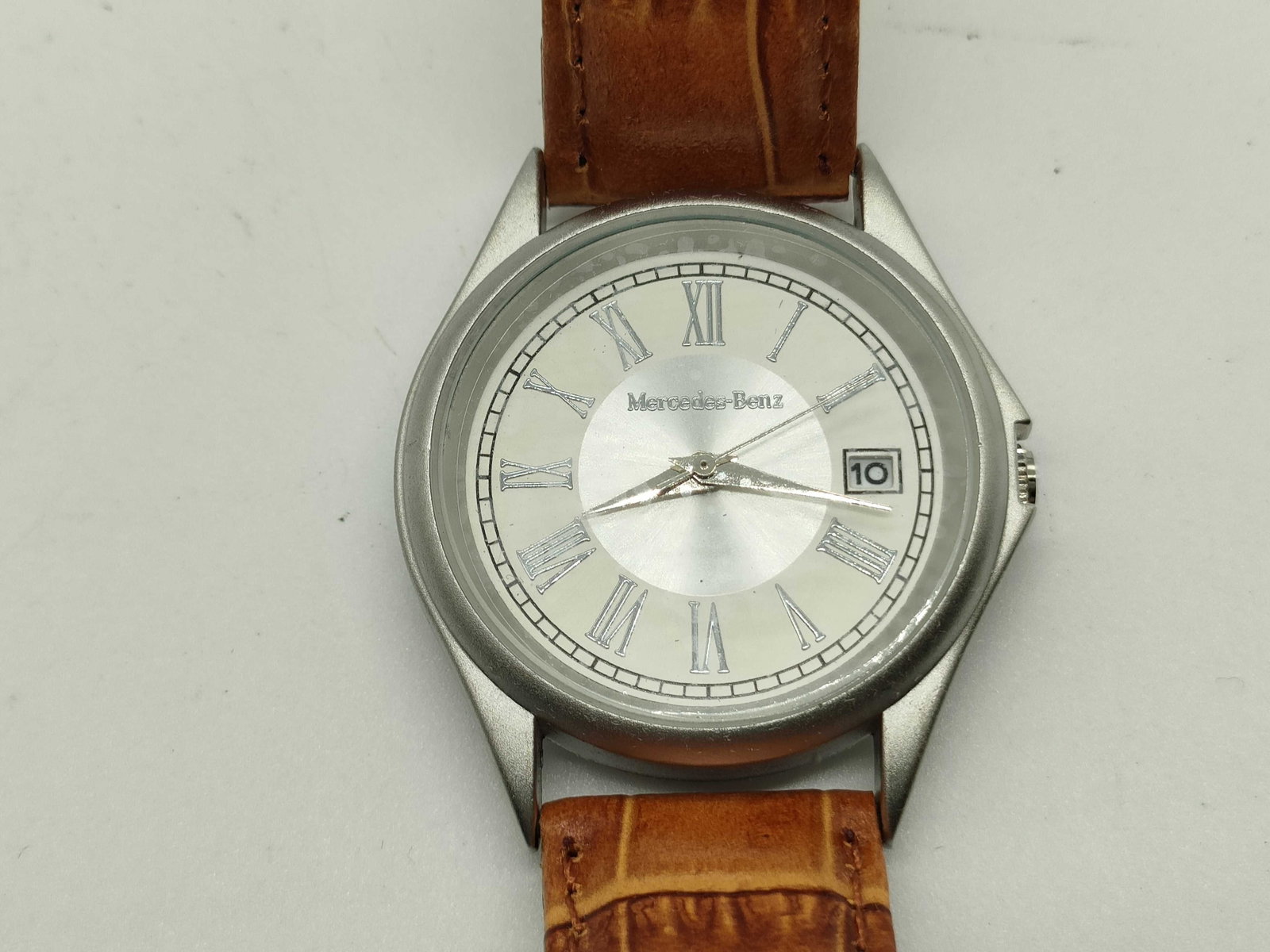 Mercedes-Benz Silver Dial Men’s Wristwatch 34mm: Mercedes-Benz men’s wristwatch having a round stainless steel case with polished bezel and silver dial. Featuring Roman numeral hour markers, date window at three o’clock, and Mercedes-Benz logo a