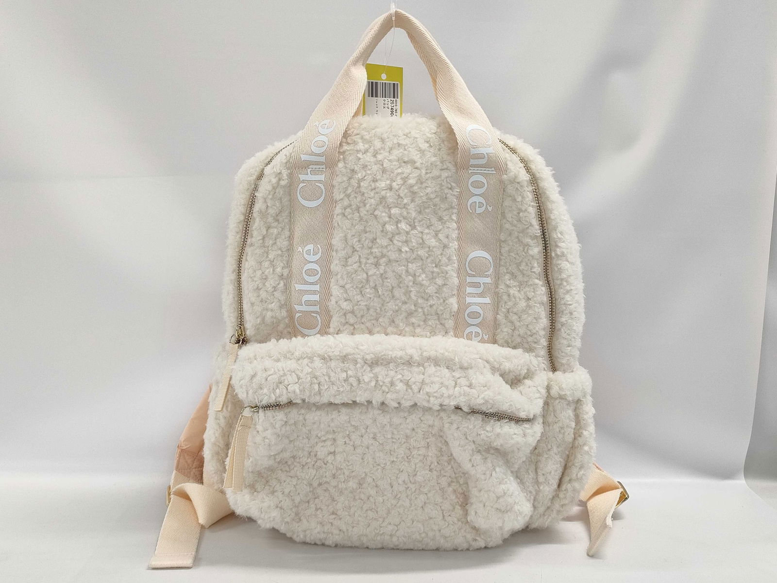 Authentic Chloé Woody Shearling Backpack: Authentic Chloe backpack in ivory/cream shearling with soft rounded silhouette. Front zip pocket with flap edge. Top handle and padded shoulder straps in beige fabric. Vertical logo webbing straps rea